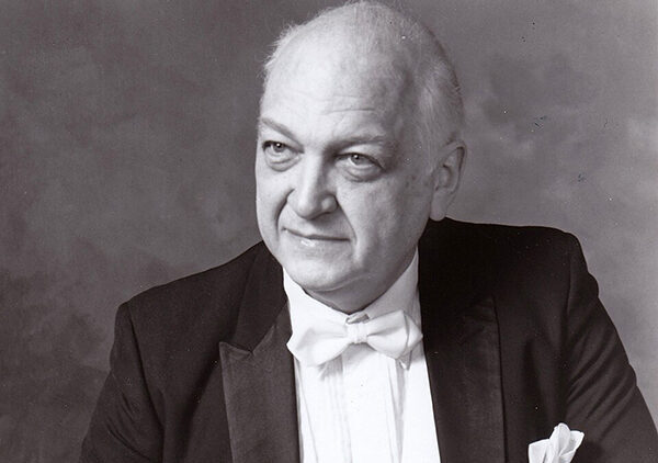 A black-and-white portrait of an older man in formal attire, wearing a tuxedo and bow tie, looking slightly to his left with a neutral expression.