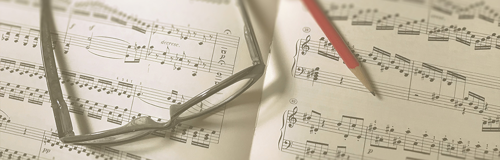 Sheet music spread out with a pair of glasses resting on one page and a red pencil placed across another page, suggesting music composition or study.