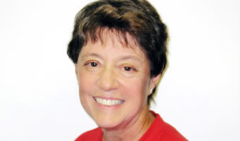 A woman with short brown hair smiles at the camera, wearing a red shirt and posing in front of a plain white background.
